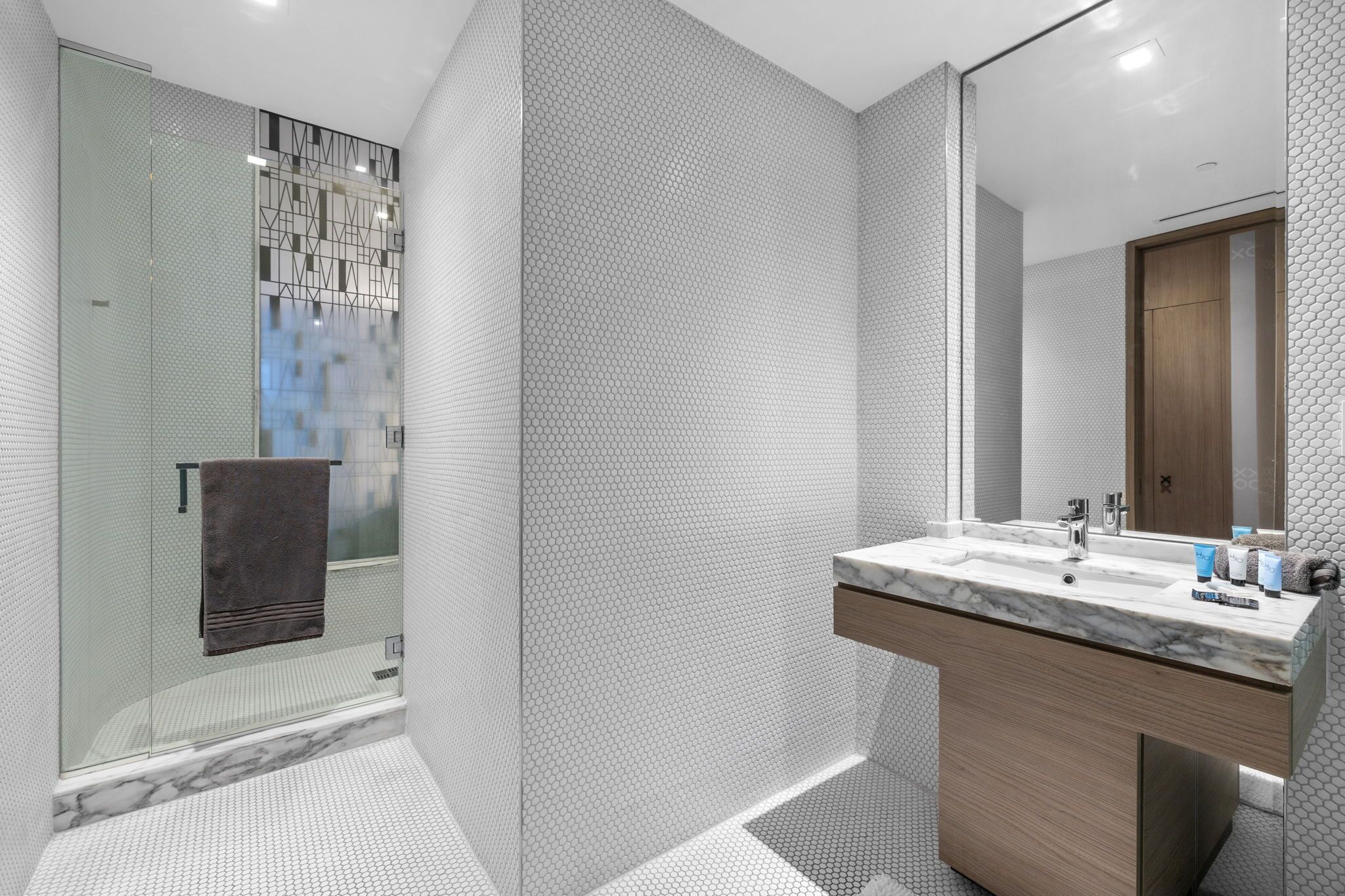 A modern bathroom with a glass shower enclosure, a marble sink, and a wooden vanity.