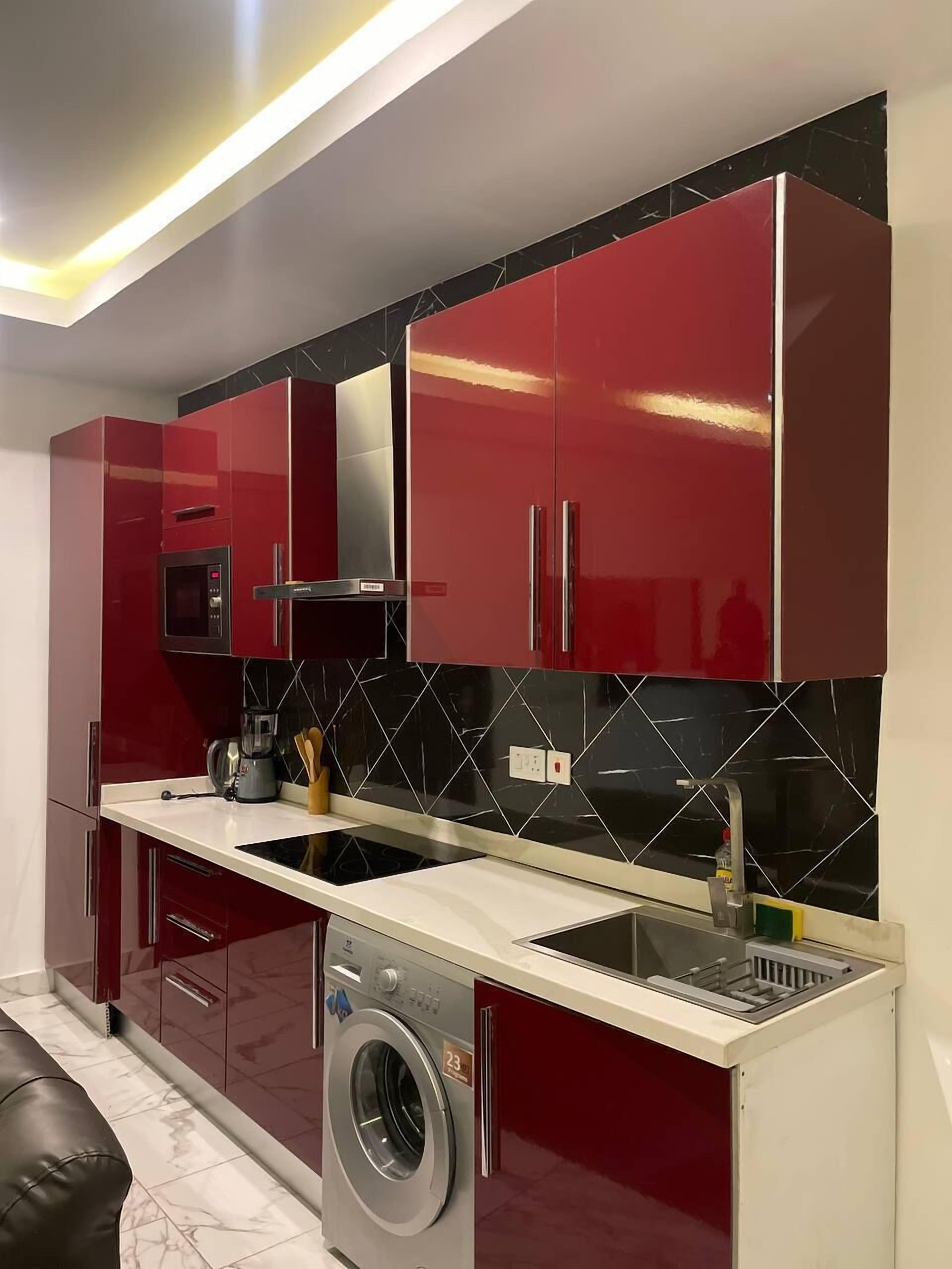 Une cuisine compacte avec des meubles rouges, un four à micro-ondes encastré et un lave-linge.