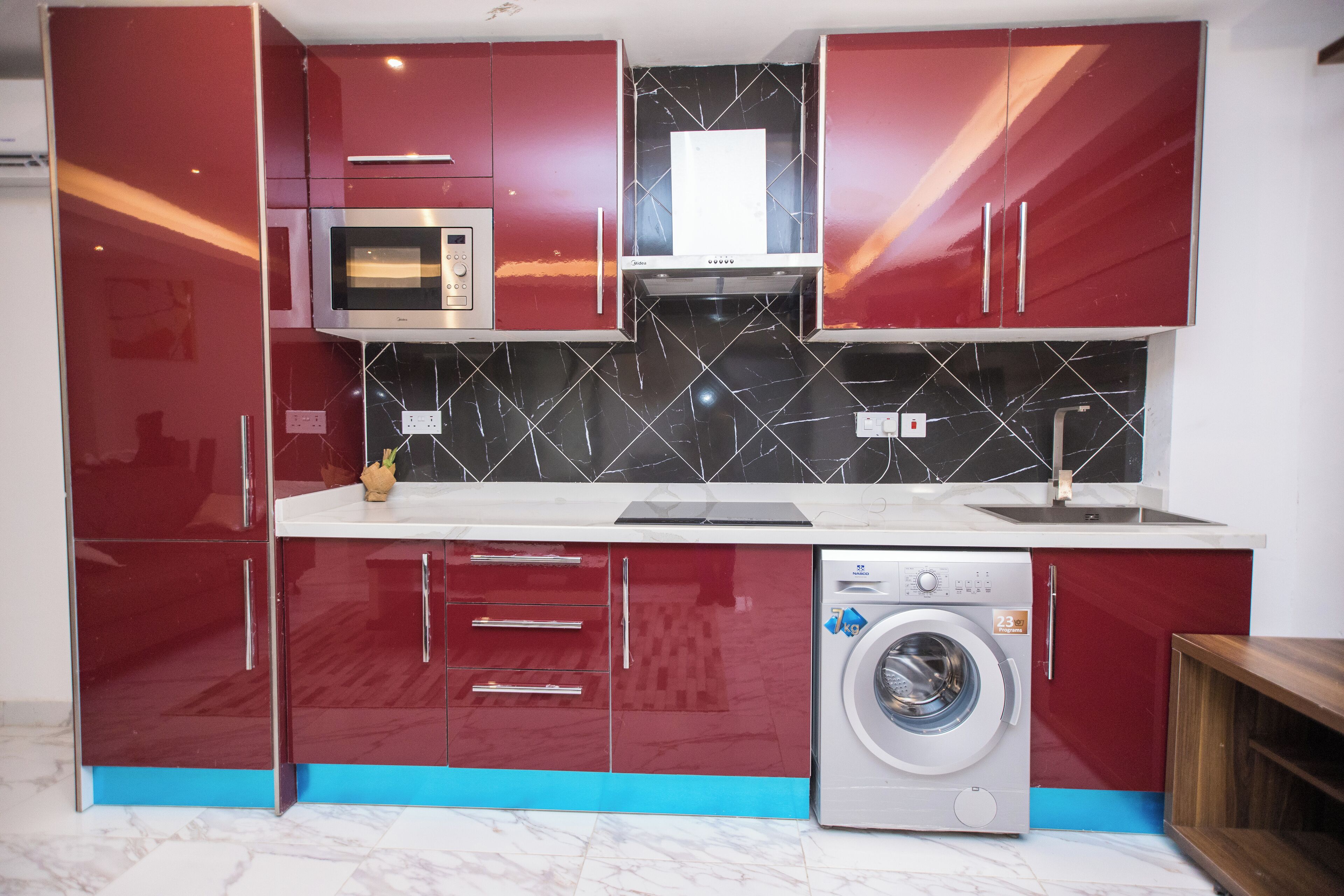 Una cocina compacta con armarios rojos, microondas, lavadora y salpicadero de azulejos.
