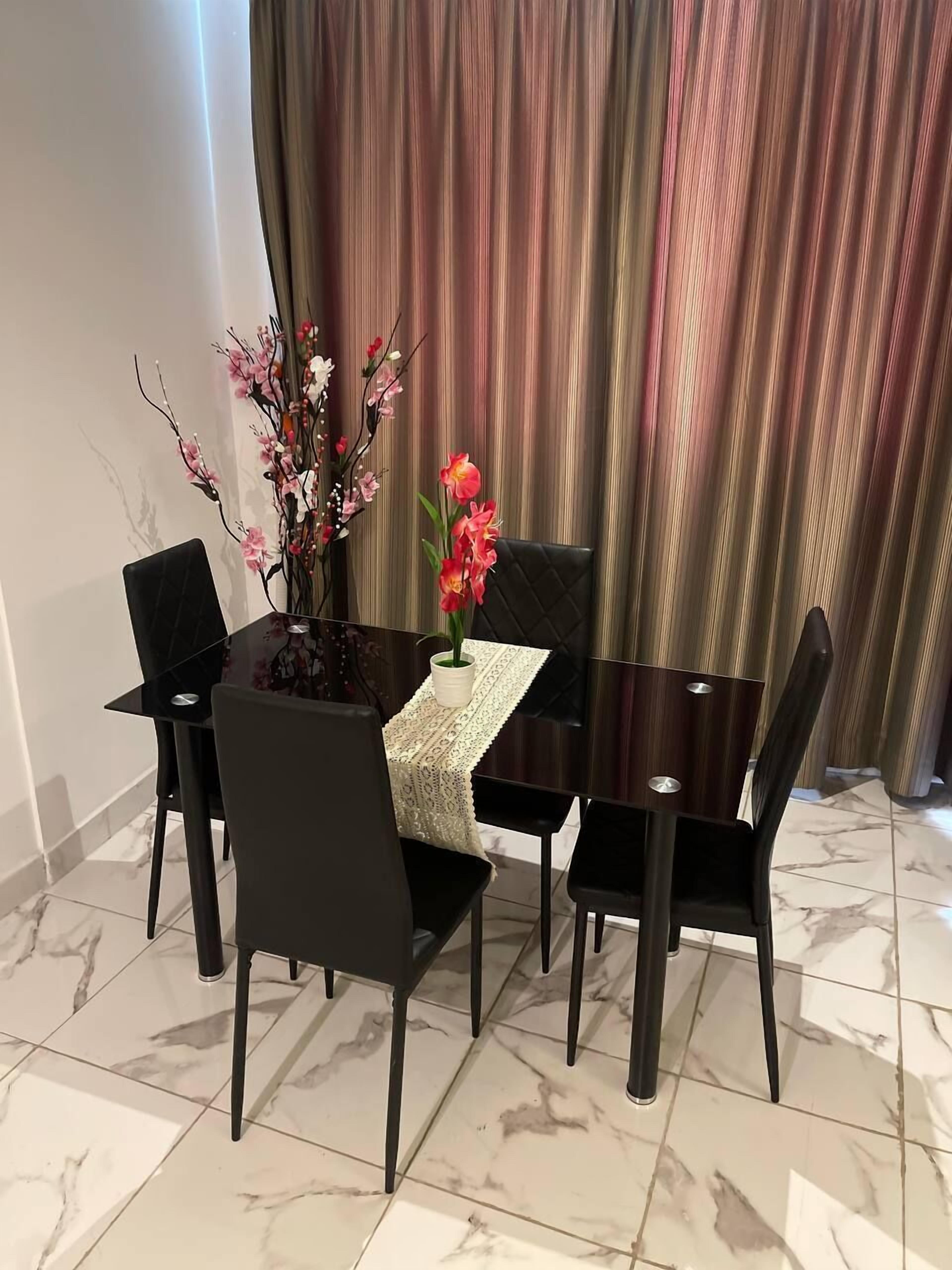 Ein Essbereich mit Marmorfliesen, einem schwarzen Esstisch und vier schwarzen Stühlen. Auf dem Tisch steht eine Vase mit rosa Blumen.