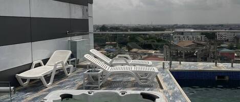A rooftop pool area with lounge chairs and a hot tub.