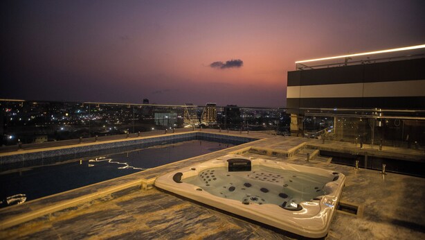 Una piscina en la azotea con jacuzzi y vista a la ciudad al atardecer.