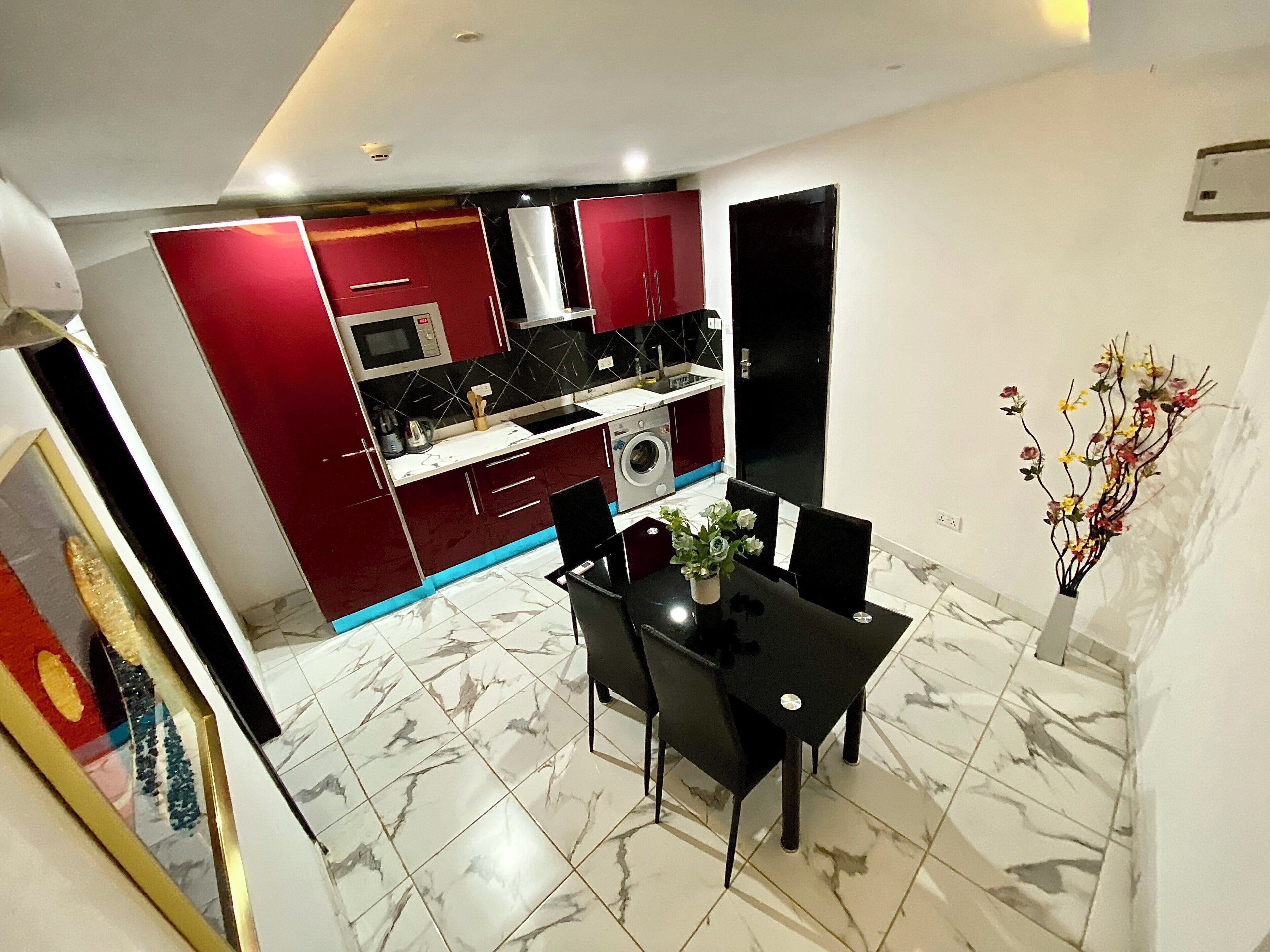 Una cocina moderna con armarios rojos, encimera negra y zona de comedor con mesa y sillas negras.