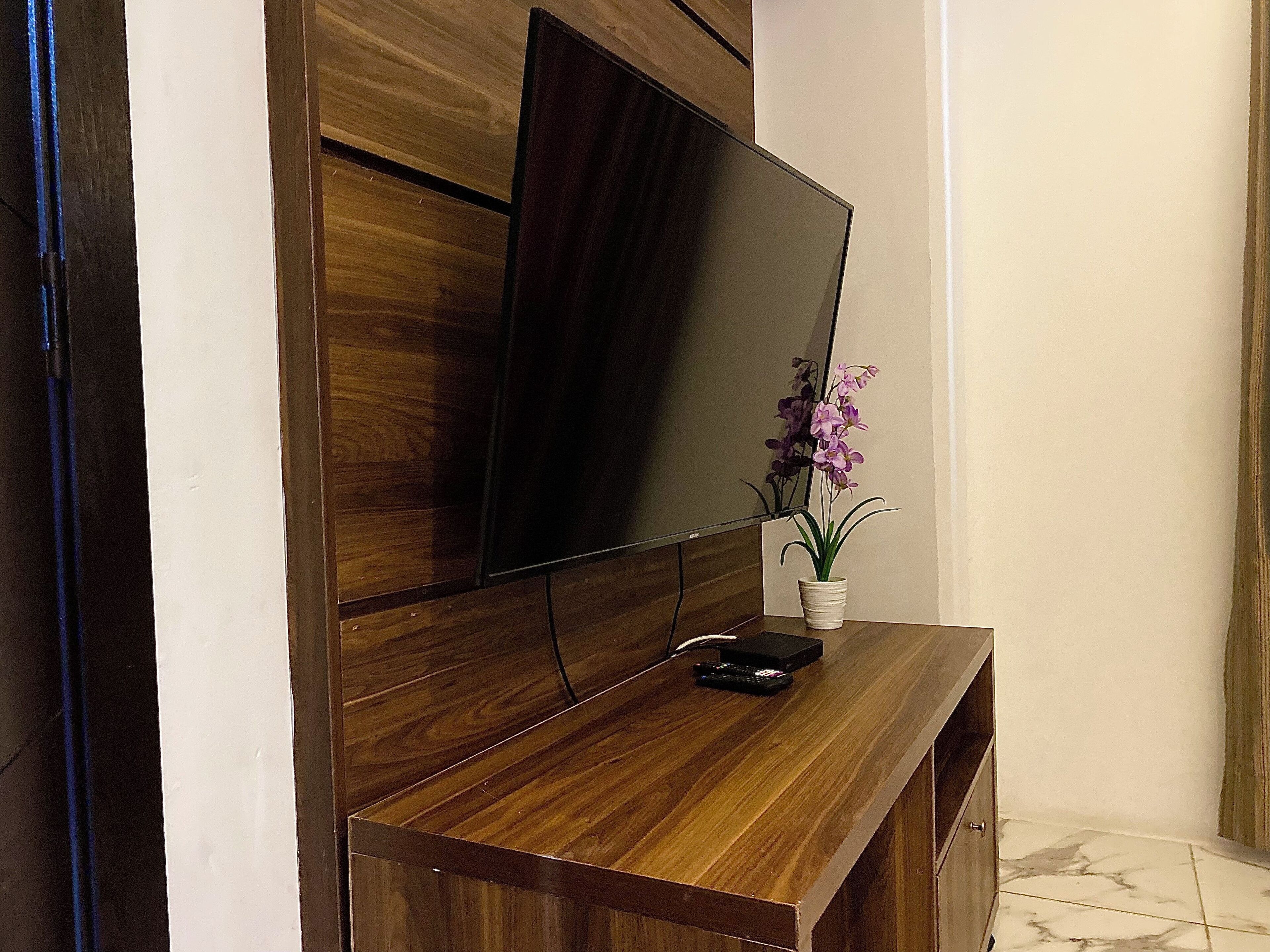 A wooden entertainment unit with a flat-screen TV, a remote control, and a potted orchid.