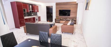 A modern living room with a dining area, a kitchen, and a TV mounted on the wall.