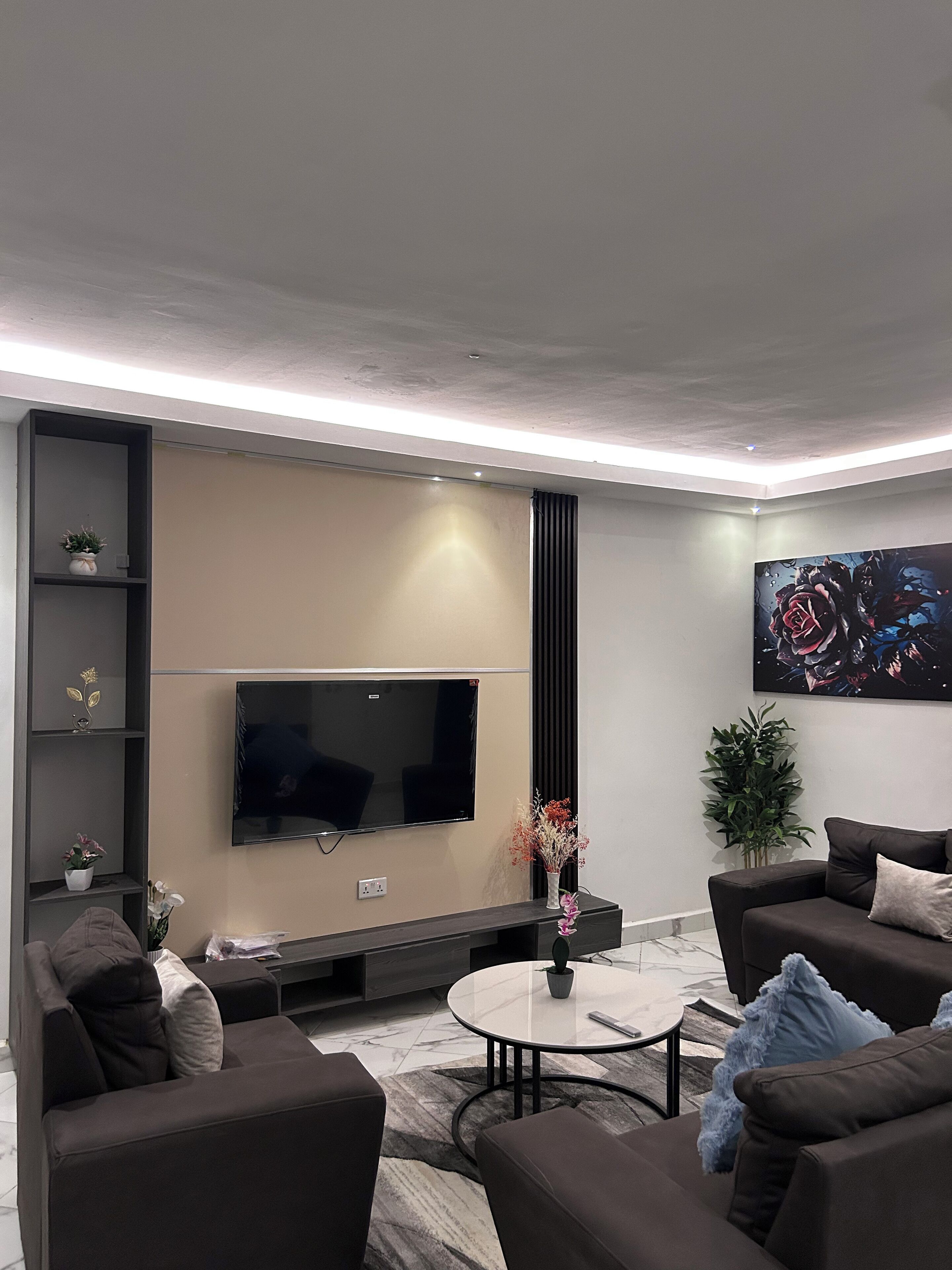 Un soggiorno moderno con televisore a schermo piatto, divani scuri, un tavolino da caffè e piante decorative.