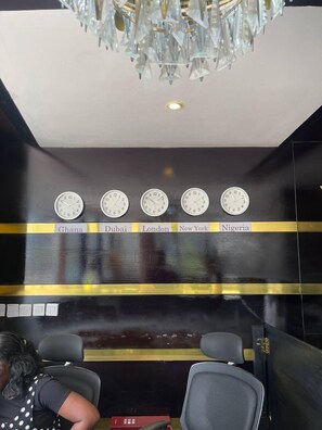 A lobby with a chandelier, clocks labeled with city names, and two chairs. - BOT PROPERTIES (Accra)