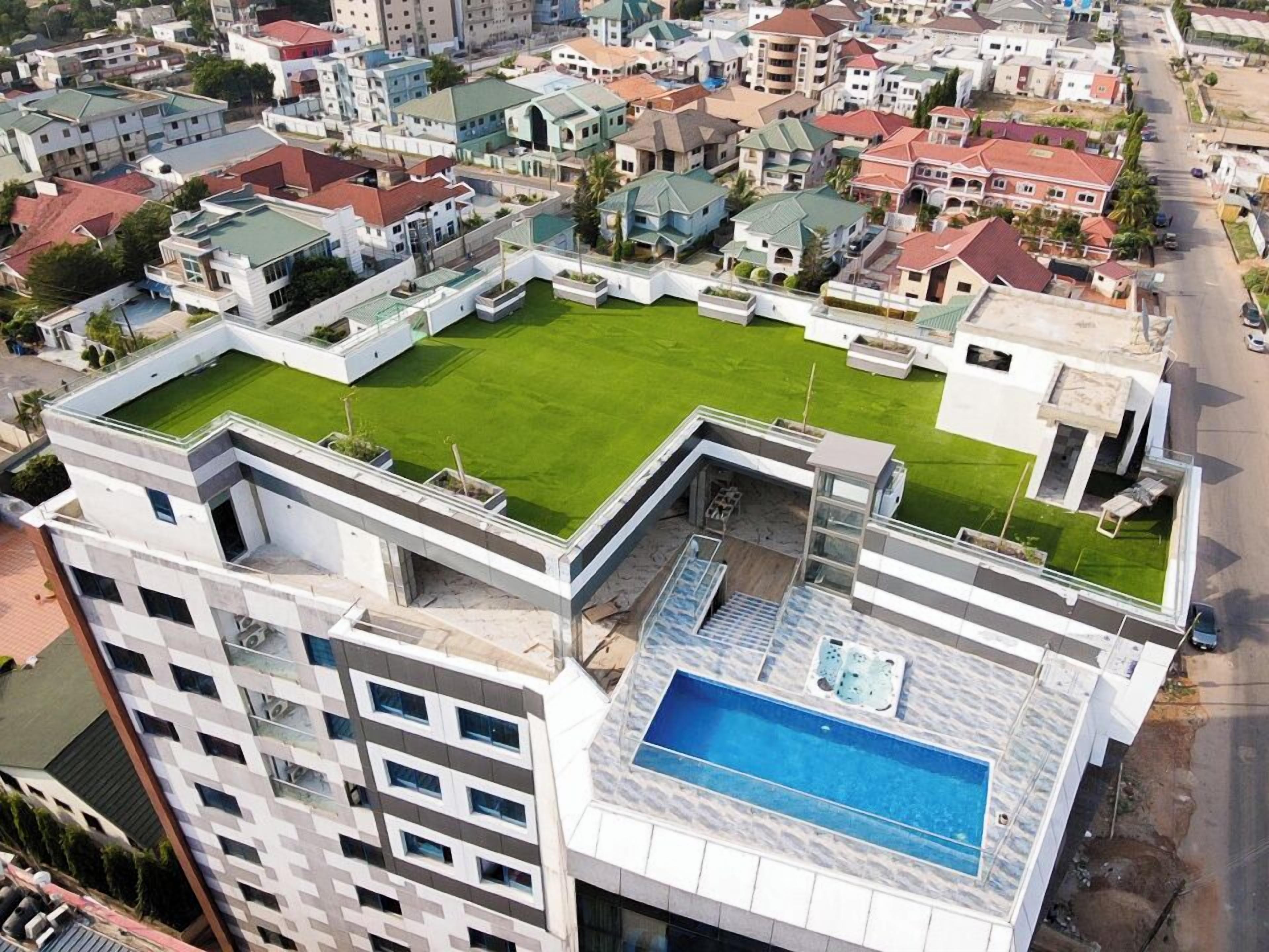 A modern high-rise building with a rooftop garden, a swimming pool, and a tennis court.