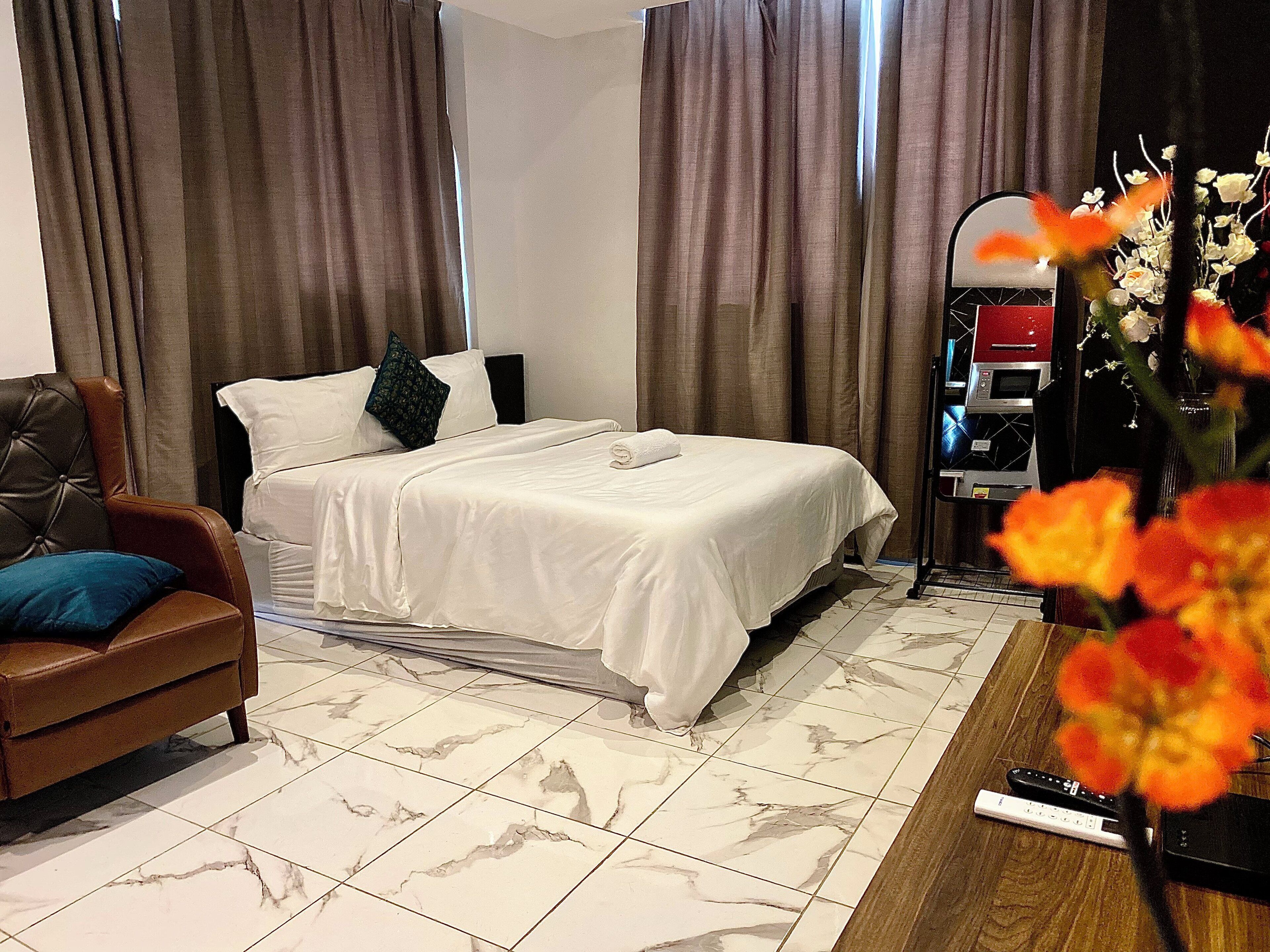 Ett hotellrum med en säng, en fåtölj i läder, ett TV-bord med en mikrovågsugn och en vas med blommor.