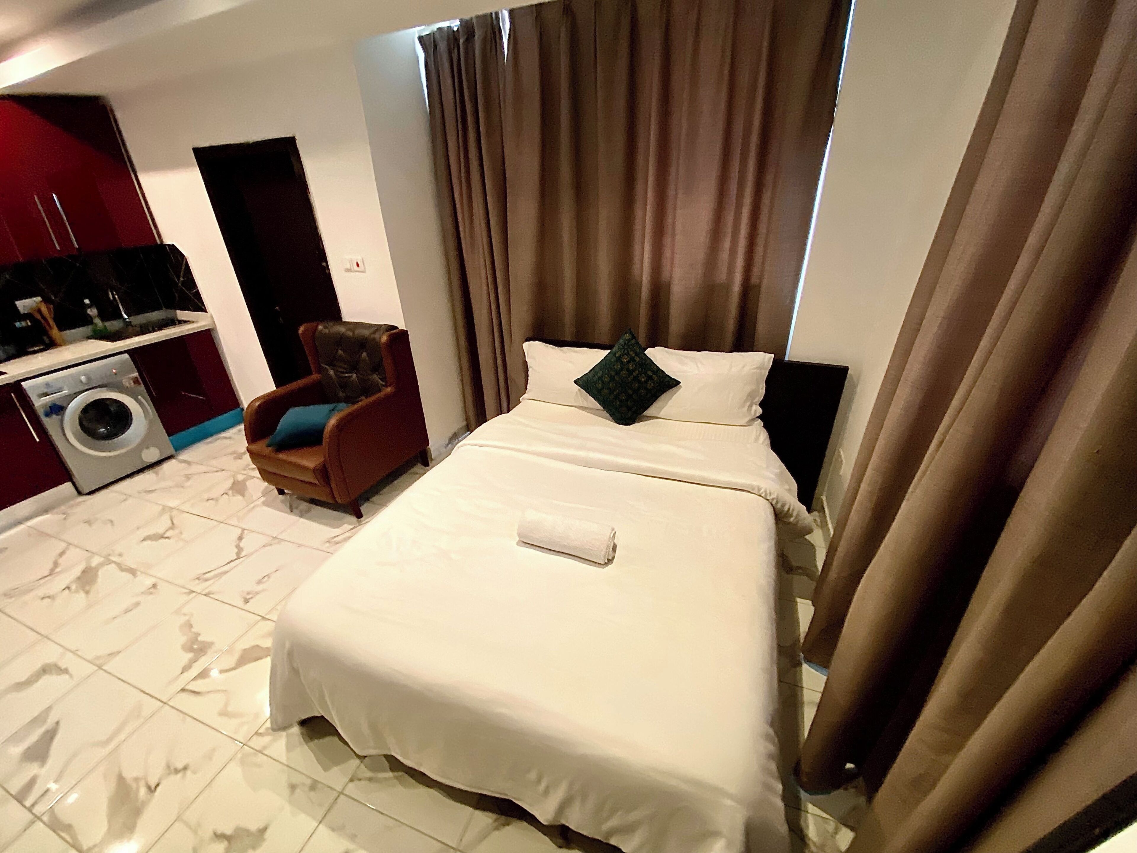 A hotel room with a bed, a chair, a washing machine, and a TV.