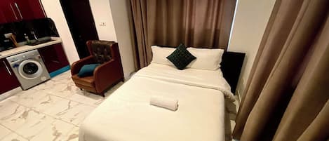 A hotel room with a bed, a chair, a washing machine, and a TV.