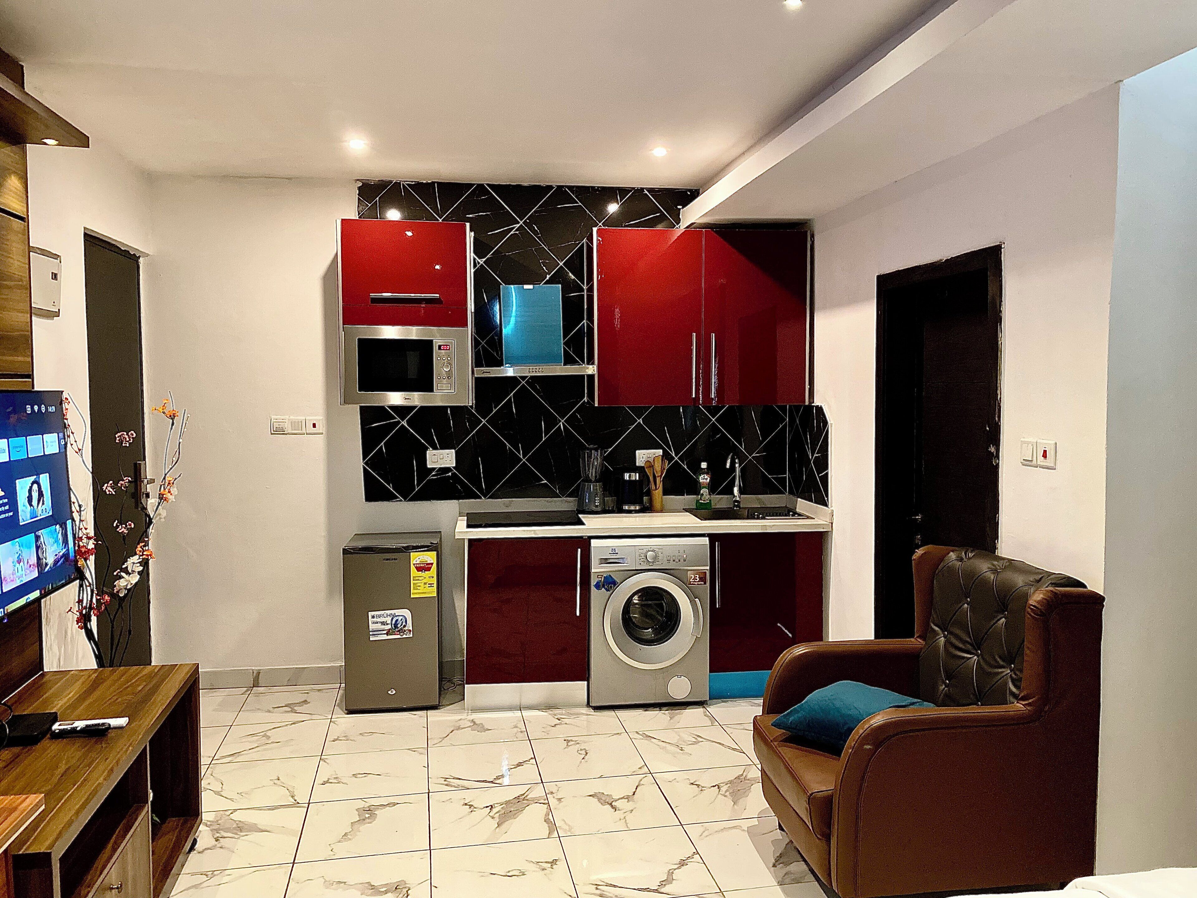 Een knus woongedeelte met een kitchenette, een wasmachine, een televisie en een leren bank.