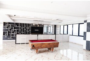 A modern indoor pool table in a spacious room with a geometric wall design, a large window, and a chandelier. - BOT PROPERTIES (Accra)