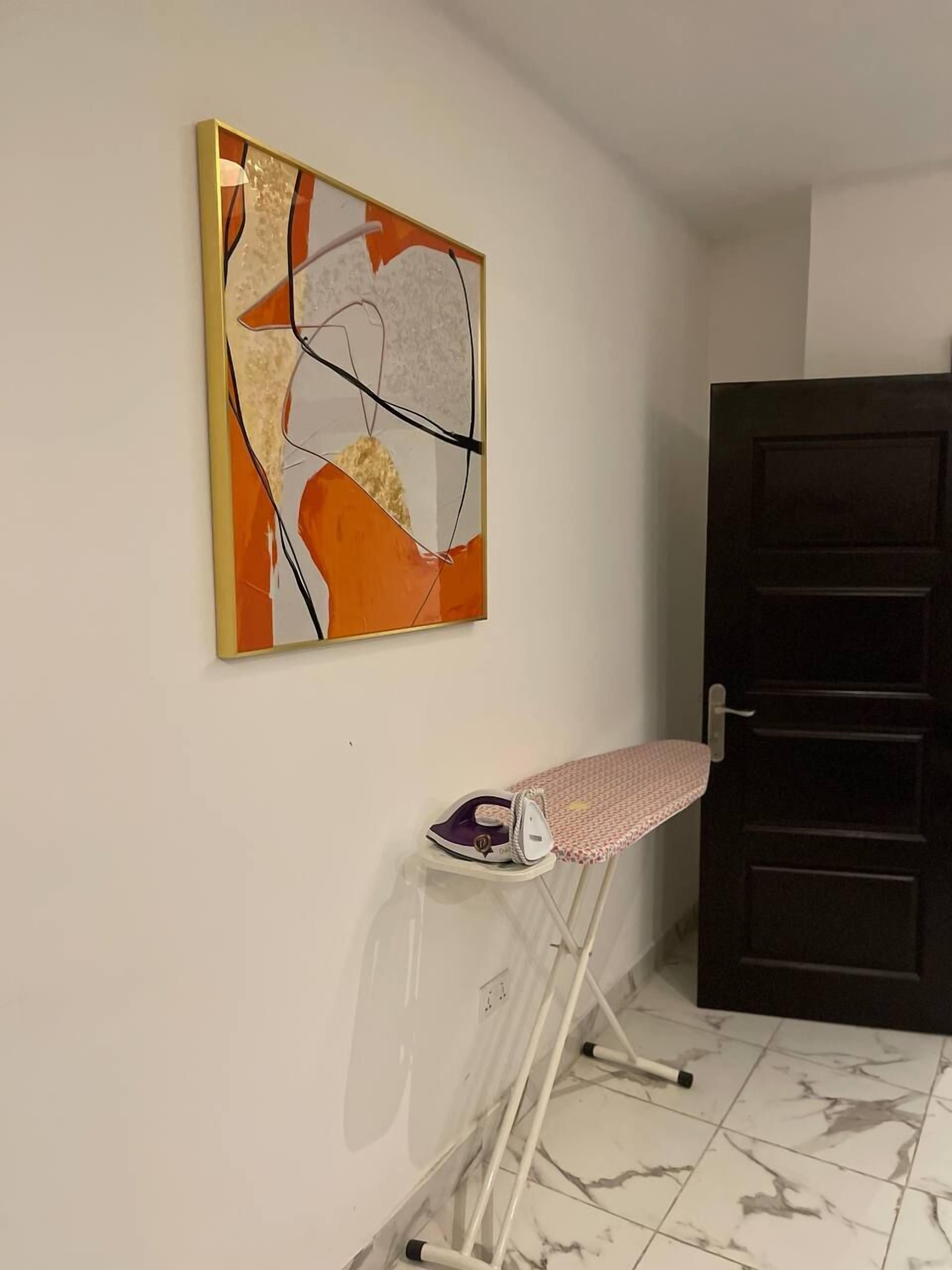 A room with a marble floor, a dark door, and a wall-mounted ironing board with an iron.