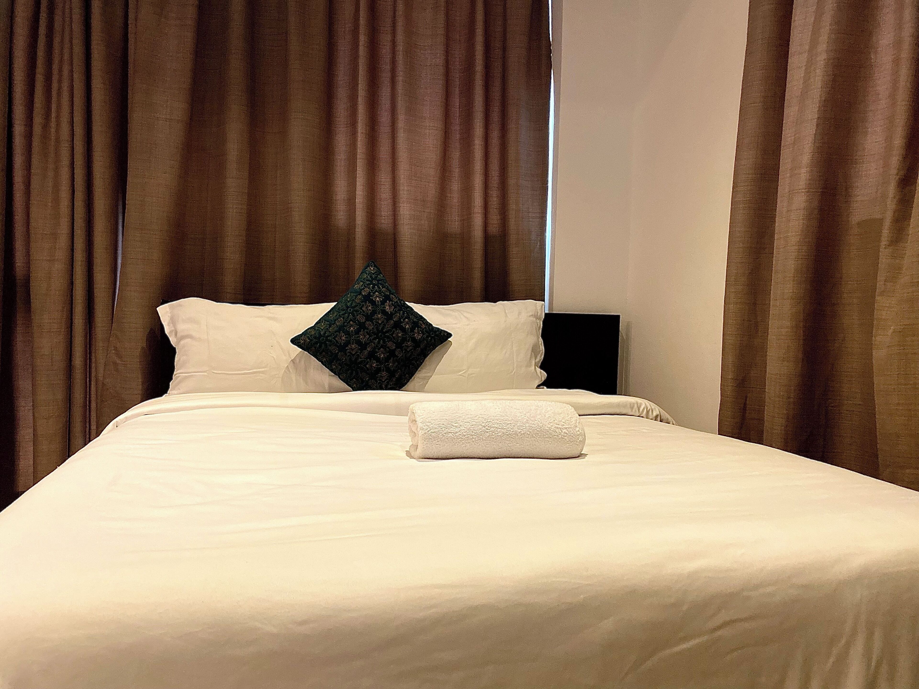 Una cama bien hecha con sábanas blancas, una almohada verde oscuro y una toalla blanca doblada.