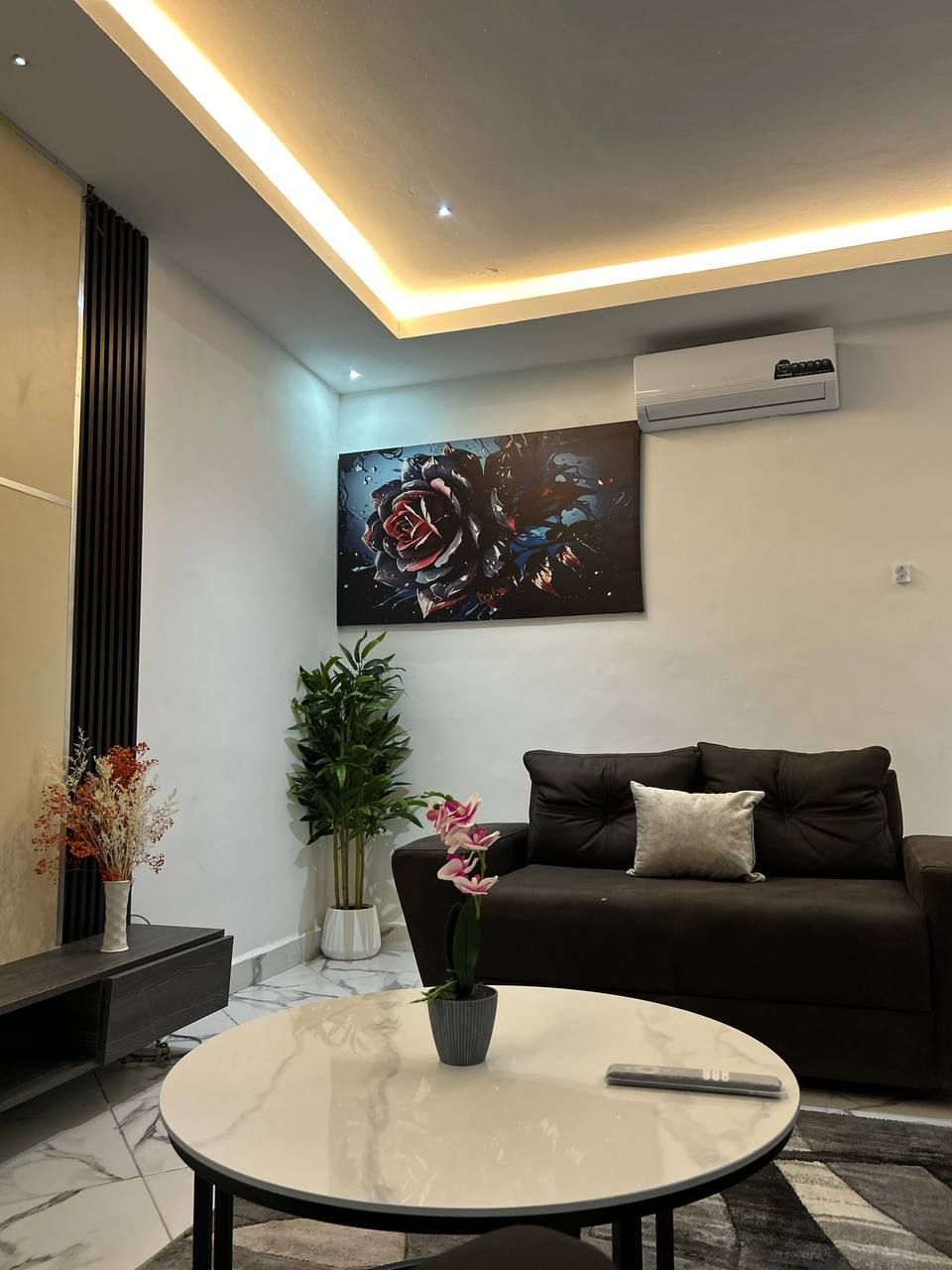 A modern living room with a dark brown sofa, a round marble coffee table, and a large abstract painting of a rose.