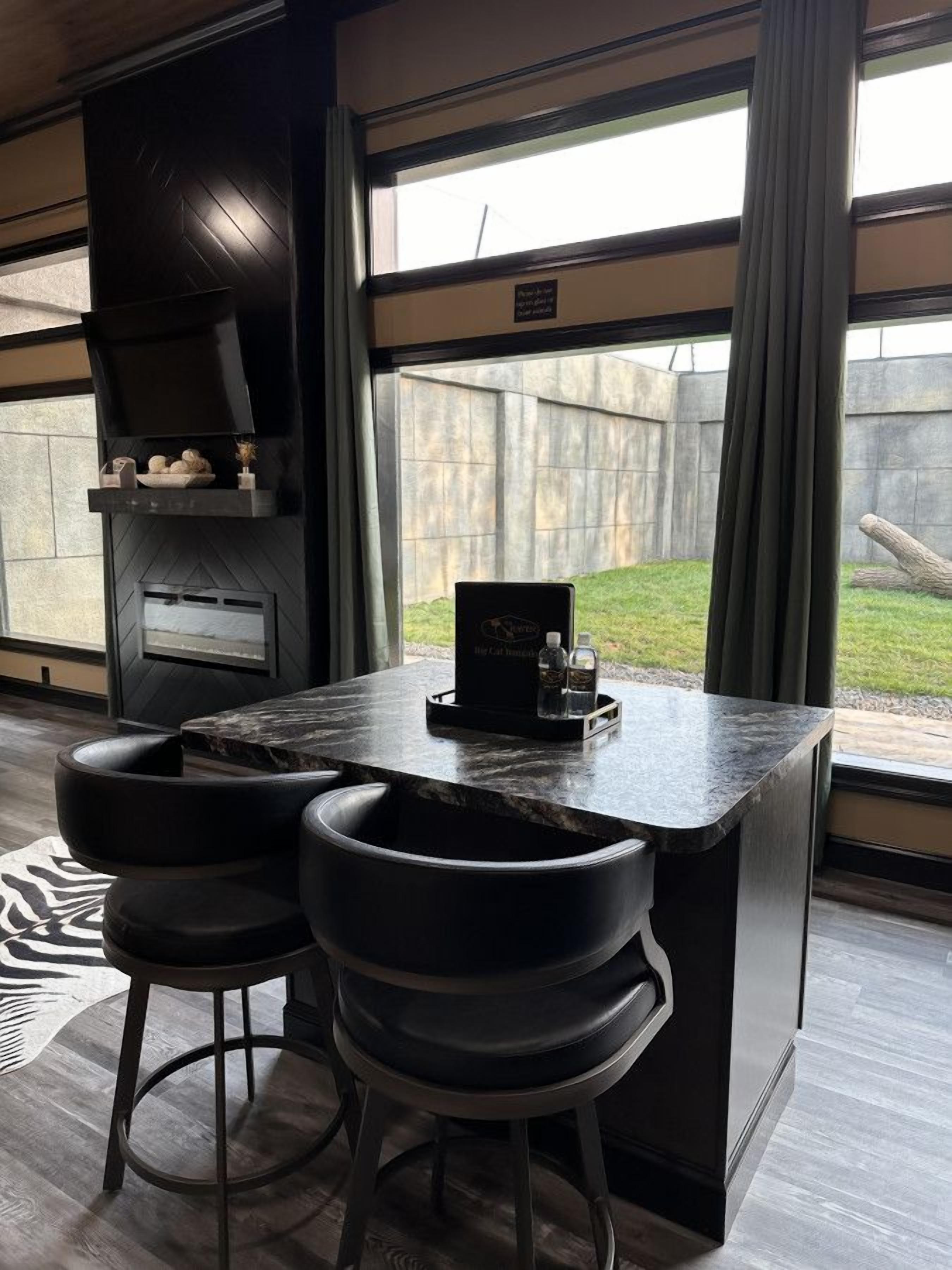 Une cuisine moderne dotée d’un barbecue intégré, de deux tabourets de bar et offrant une vue sur le jardin arrière.