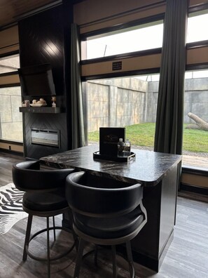 A modern kitchen with a built-in grill, two bar stools, and a view of the backyard. - Big Cat Bungalows at The Haven (Chittenango)