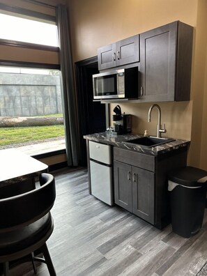 Cocina compacta con muebles oscuros, microondas integrado, cafetera y lavamanos.