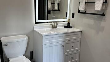 A modern bathroom with a white toilet, a vanity with a mirror, and a towel rack.