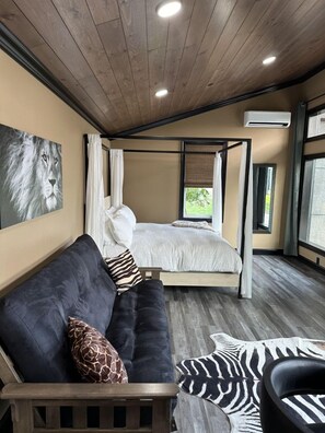 A bedroom with a bed, a sofa, and a zebra-patterned rug. - Big Cat Bungalows at The Haven (Chittenango)