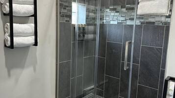 Et moderne bruseområde med glasdør, mørke fliser og et håndklædestativ med foldede håndklæder.