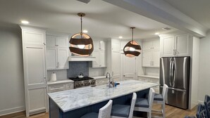Una cocina moderna con armarios blancos, una isla de mármol, dos lámparas colgantes y un refrigerador de acero inoxidable.