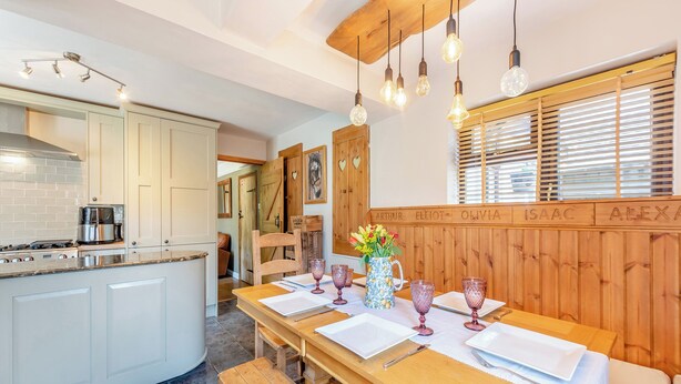 Une cuisine moderne avec des meubles blancs, une table à manger en bois mise avec des assiettes, des verres et un vase de fleurs.