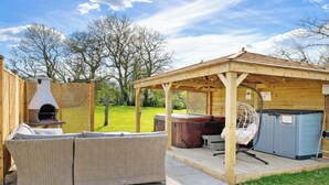 Un espace extérieur aménagé, abrité et doté d’un jacuzzi, d’une pergola en bois et d’une table de patio.