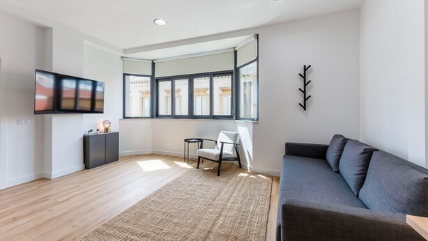 A modern living room with a large window, a flat-screen TV, a grey sofa, and a small table with a lamp. - Charming 1Bdr Flat in Central Faro by Lovelystay (Faro)