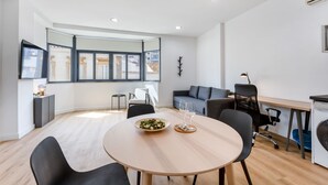 A modern living room with a round wooden table, a grey sofa, and a large window with a view of buildings. - Charming 1Bdr Flat in Central Faro by Lovelystay (Faro)