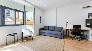 A modern, well-lit room with a grey sofa, a white chair, a desk with a computer, and a TV. - Charming 1Bdr Flat in Central Faro by Lovelystay (Faro)