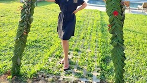 A person standing under a large, leaf-woven arch in a grassy outdoor area with a building in the background. - Campo Verde Lodge (Campoverde)