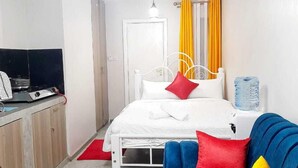 Ein Schlafzimmer mit einem Bett, einem blauen Sofa mit roten und gelben Kissen, einem roten Teppich, einer weißen Tür und einem weißen Heizkörper.