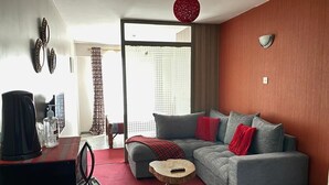 Ein modernes Wohnzimmer mit grauem Sofa, roten Kissen, einem kleinen Holztisch und einer roten Pendelleuchte.