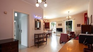 A spacious living room with a wooden coffee table, a TV, and a fireplace. There is a dining area with chairs and a table, and a kitchen area with a refrigerator and a sink.