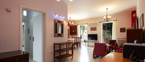 A spacious living room with a wooden coffee table, a TV, and a fireplace. There is a dining area with chairs and a table, and a kitchen area with a refrigerator and a sink.