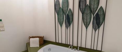 Ein modernes Badezimmer mit einer freistehenden Badewanne, einem Holzbadezimmer-Möbelstück und einer gerahmten Blattform-Kunstwerk über der Wanne.