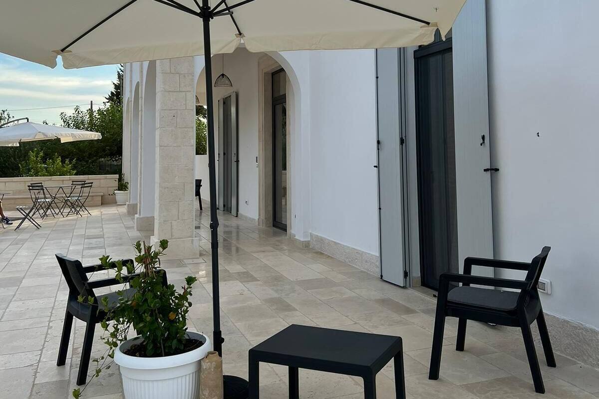 An outdoor patio with a white umbrella, two black chairs, a small table, and a potted plant.