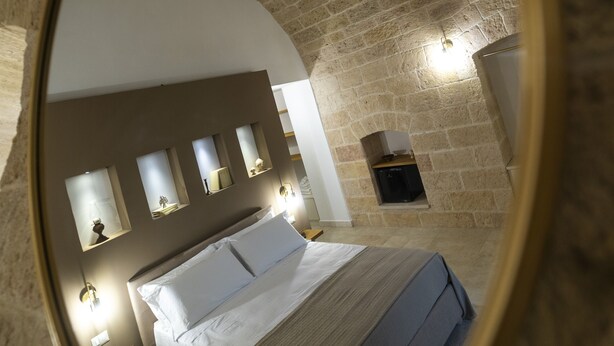 A circular mirror reflecting a bedroom with a bed, bedside tables, and wall-mounted lights. - Dimora CARASPI  (Mola di Bari)