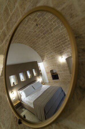 A circular mirror reflecting a bedroom with a bed, bedside tables, and wall-mounted lights. - Dimora CARASPI  (Mola di Bari)