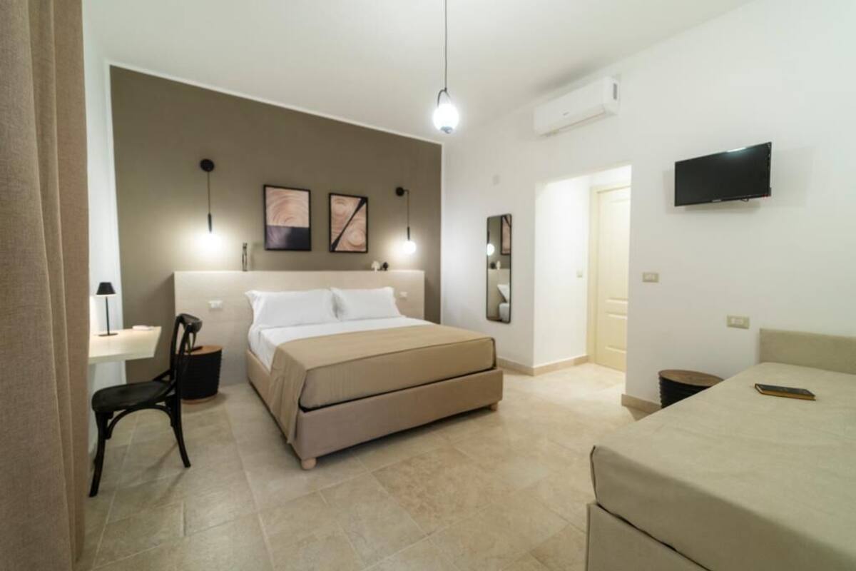 A bedroom with a bed, a desk, a chair, a TV, and artwork on the wall.