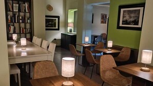 A modern dining area with wooden tables and chairs, a bookshelf, and a green accent wall. - Ultroneo locanda di collina (Vinci)