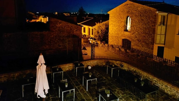 A courtyard with stone tables and chairs, a white umbrella, and a stone building with a window. - Ultroneo locanda di collina (Vinci)
