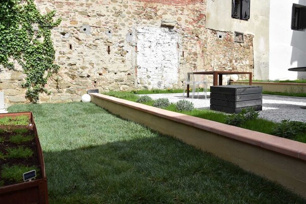 A courtyard with a stone wall, a grassy area, a wooden bench, and a planter box. - Ultroneo locanda di collina (Vinci)