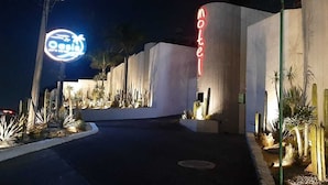 A motel with a neon sign, a well-lit entrance, and a landscaped area with cacti.