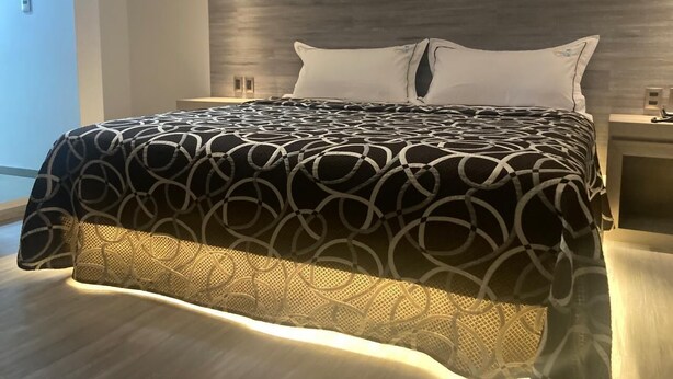 A modern bedroom with a large bed, a wooden headboard, and a nightstand with a lamp.