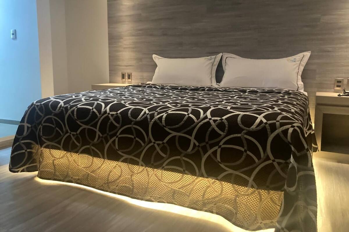 A modern bedroom with a large bed, a wooden headboard, and a nightstand with a lamp.