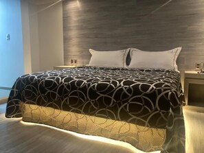 A modern bedroom with a large bed, a wooden headboard, and a nightstand with a lamp. - Hotel Oasis (Tlalnepantla de Baz)