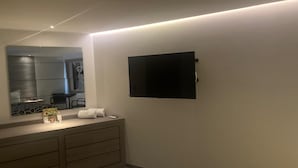 A modern bathroom with a large mirror, a flat-screen TV mounted on the wall, and a wooden vanity with drawers.